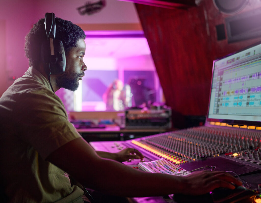 Black man, studio recording and music job in night with headphones, computer or focus by mixing con.